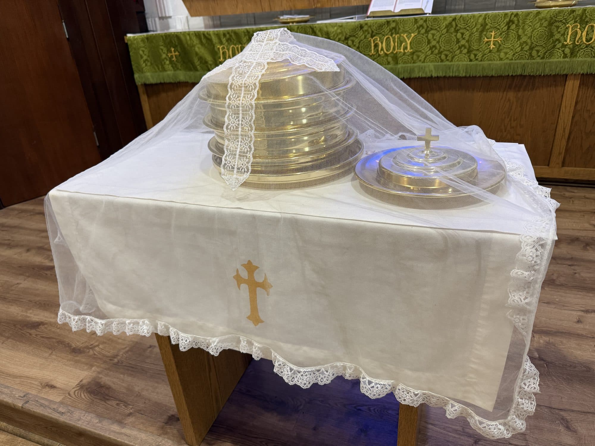 The communion vessels set out on the credence table under a lace veil, with the green altar paraments behind
